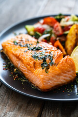 Fried salmon fillet with fried potatoes, lime and vegetable salad served on black plate on wooden table

