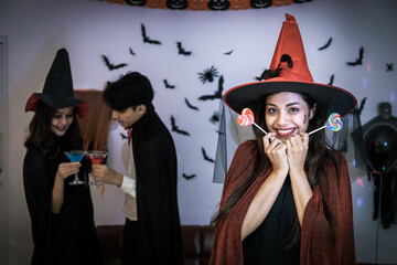 Portrait of young Asian woman smiling in Halloween costumer as witch in party, holding candy,...