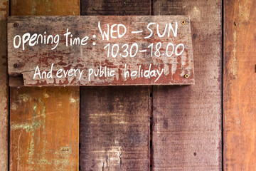 The sign indicates the closing and opening times of shops and locations, it is written in white letters on an old wooden wall.