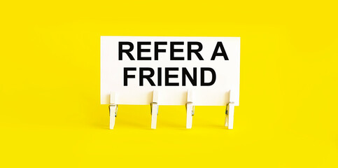 text REFER A FRIEND on white short note paper yellow background
