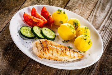 Fried chicken breast with boiled potatoes and fresh vegetables on wooden table
