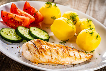 Fried chicken breast with boiled potatoes and fresh vegetables on wooden table
