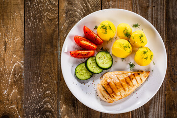 Fried chicken breast with boiled potatoes and fresh vegetables on wooden table
