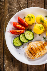 Fried chicken breast with boiled potatoes and fresh vegetables on wooden table
