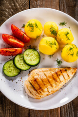 Fried chicken breast with boiled potatoes and fresh vegetables on wooden table
