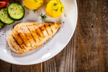 Fried chicken breast with boiled potatoes and fresh vegetables on wooden table
