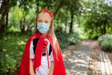 Portrait of cute Little Girl in costume of red hat in the park. Happy Halloween during coronavirus covid-19 pandemic quarantine concept. Kid wearing medical mask
