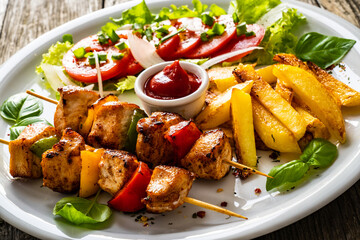 Skewers - grilled meat with French fries and fresh vegetables on wooden background