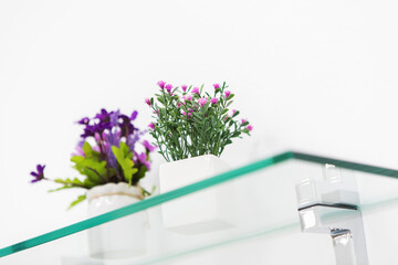 Artificial flowers in pots on a glass shelf. Home decoration