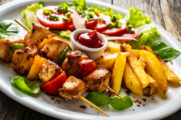 Skewers - grilled meat with French fries and fresh vegetables on wooden background