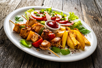 Skewers - grilled meat with French fries and fresh vegetables on wooden background