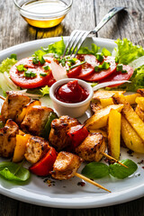 Skewers - grilled meat with French fries and fresh vegetables on wooden background