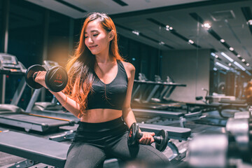 Fototapeta na wymiar Muscular young asian woman with beautiful body doing exercises with dumbbell. Sporty girl lifting weights in gym.