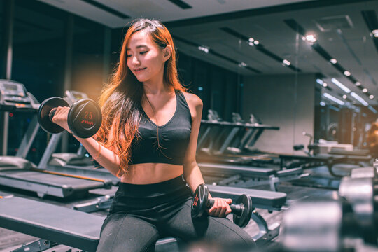 Muscular young asian  woman with beautiful  body doing exercises with dumbbell. Sporty girl lifting weights in gym.