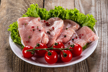 Raw pork chops with fresh lettuce and cherry tomatoes  on plate on wooden background 