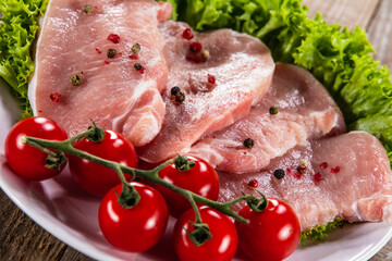 Raw pork chops with fresh lettuce and cherry tomatoes  on plate on wooden background 