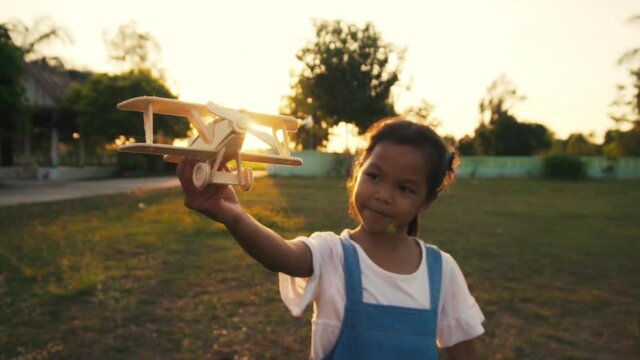Happy girl walking with a toy airplane on a yard in the sunrise light. Children dreams of flying and becoming a pilot. The concept of a happy childhood dreams. Slow motion