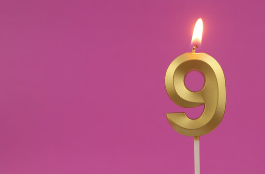 Burning golden birthday candle on pink background with copy space, number 9