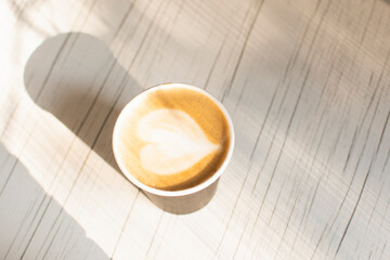 paper Cup of coffee with foam on a wooden background. milk foam heart