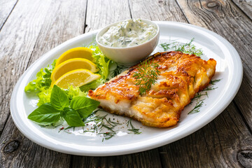Fish dish - fried cod fillet with cream sauce and lemon served on wooden table
