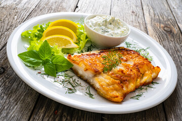 Fish dish - fried cod fillet with cream sauce and lemon served on wooden table
