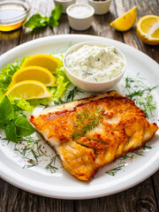 Fish dish - fried cod fillet with cream sauce and lemon served on wooden table
