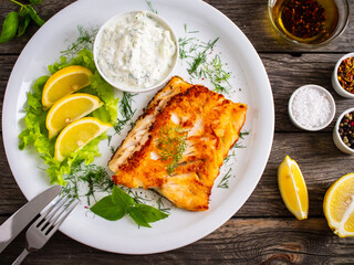 Fish dish - fried cod fillet with cream sauce and lemon served on wooden table
