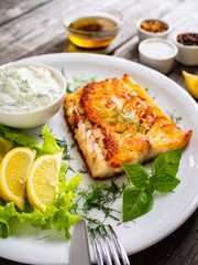 Fish dish - fried cod fillet with cream sauce and lemon served on wooden table
