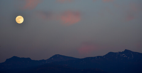 Full moon and pink clouds over the mountains