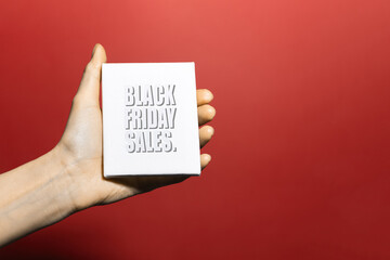 Close-up of black friday text on white paper in female hand. Background of red color.