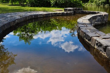 Naklejka premium Water Reflection in Pond of Blue Sky with Clouds and Green Tree in Czech Park.