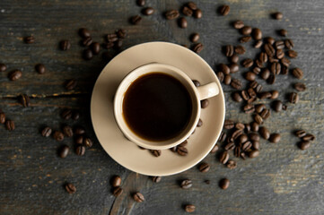 Coffee cup with roasted coffee beans on wooden table background. Mug of black coffe with scattered coffee beans on a wooden table. Fresh coffee beans.