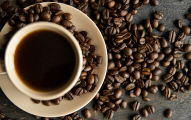 Coffee cup with roasted coffee beans on wooden table background. Mug of black coffe with scattered coffee beans on a wooden table. Fresh coffee beans.