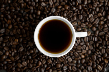 White cup of coffee with roasted coffee beans background. Mug of black coffee.