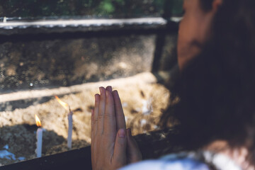 Woman praying and burning candles in the garden of the Virgin Mary house. Burning white candles on stand. Worship