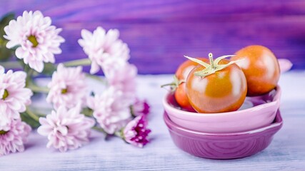 Ripe tomatoes and pink chrysanthemums on purple wooden background, 16 on 9 format