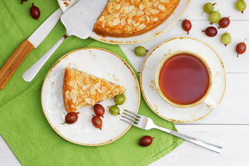 Homemade gooseberry pie garnished with almond petals and cup of tea on white wooden table. Top view.