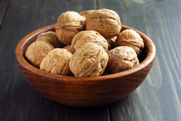 Walnuts in a wood bowl and on a dark wooden table