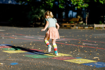 Naklejka premium Cute little toddler girl playing hopscotch game drawn with colorful chalks on asphalt. Little active child jumping on playground outdoors on a sunny day. Summer activities for children.