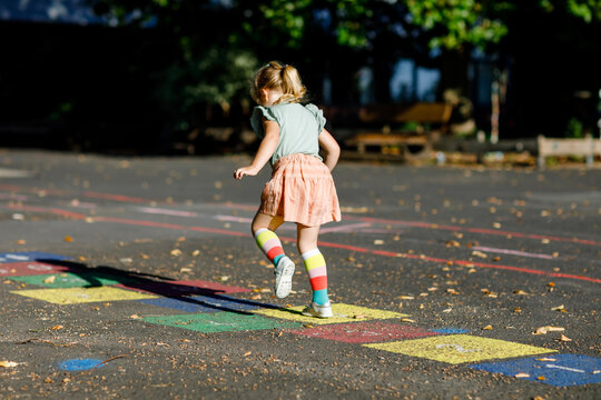 Cute little toddler girl playing hopscotch game drawn with colorful chalks on asphalt. Little active child jumping on playground outdoors on a sunny day. Summer activities for children.