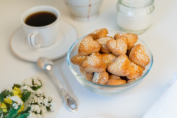 small heart-shaped shortbread cookies sprinkled with sesame seeds in a glass bowl, a cup of black coffee, sugar and wildflowers - breakfast still life