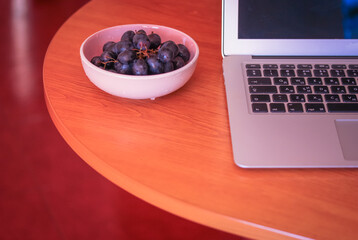 Desktop: laptop and plate with blue grapes on a wooden surface