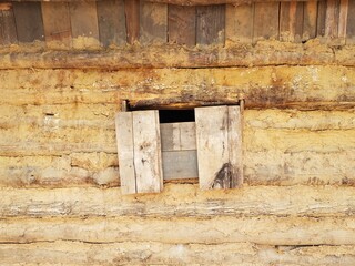 boarded window on old log and mud cabin