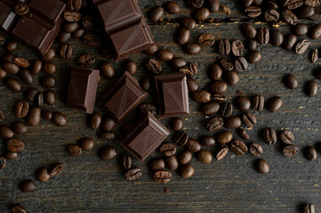 Roasted arabica coffee beans scattered on a wooden table with a bar of dark chocolate. Fresh coffee beans.