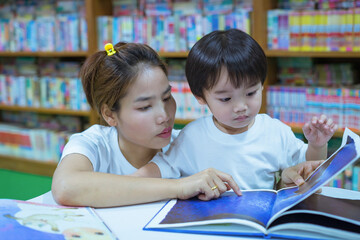 Asian young mother with little boy reading book together in library. Happy family. Parent educating children. Pre-school learning concept.