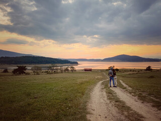 Two persons are watching the scenic sunset near the dam.