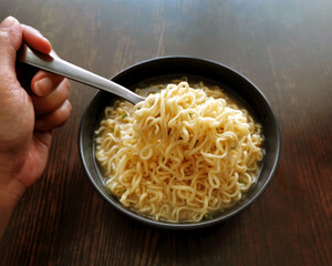 Instant noodles on a black bowl with hand holding a fork on the left side. 