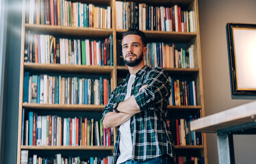 Smiling young bearded man looking away while standing in bookstore