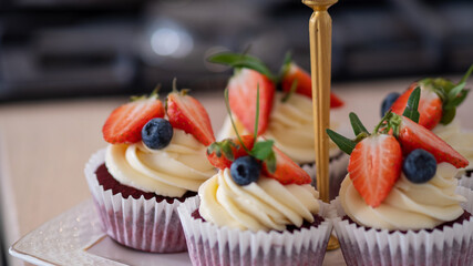 Delicious sweet muffins with cream, decorated with strawberries and blueberries.