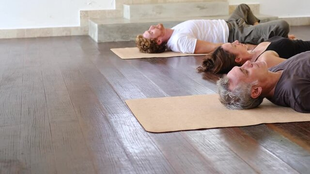 Diverse group of people on wooden floor practicing yoga lying in Reclined Butterfly exercise relaxing after practice. Healthy lifestyle